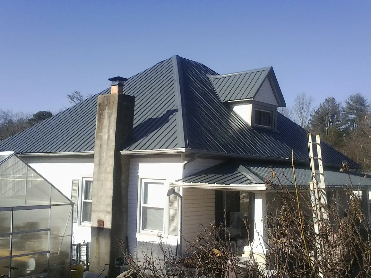 Dark blue standing seam metal roof on a white farmhouse with dormer — Slate & Tile Roof Repair by Roofing Brothers in Las Animas