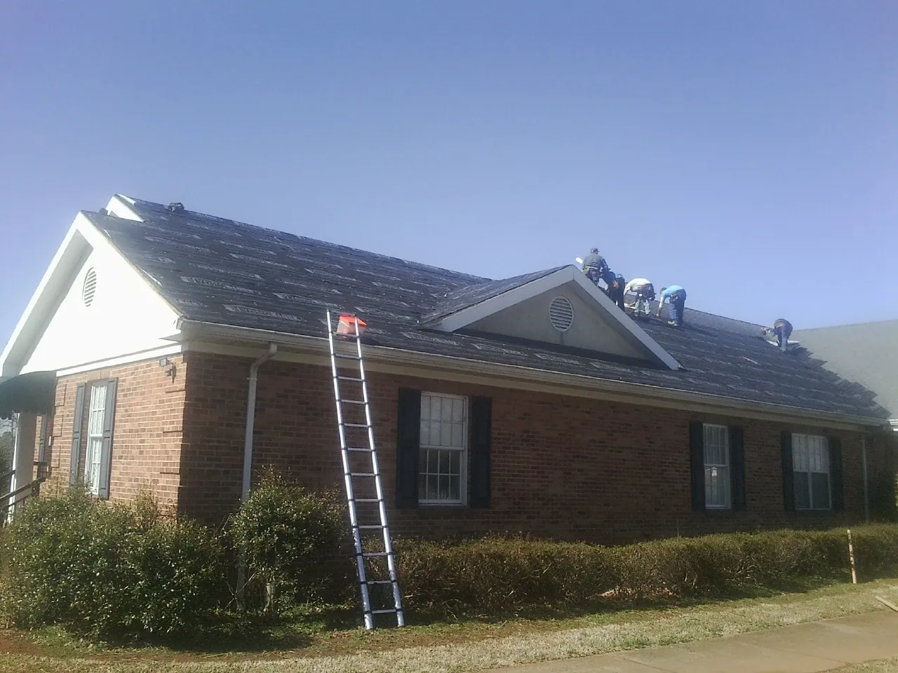 Crew tearing shingles off a brick ranch roof with a ladder set — Metal Roof Repair work by our crew in Las Animas