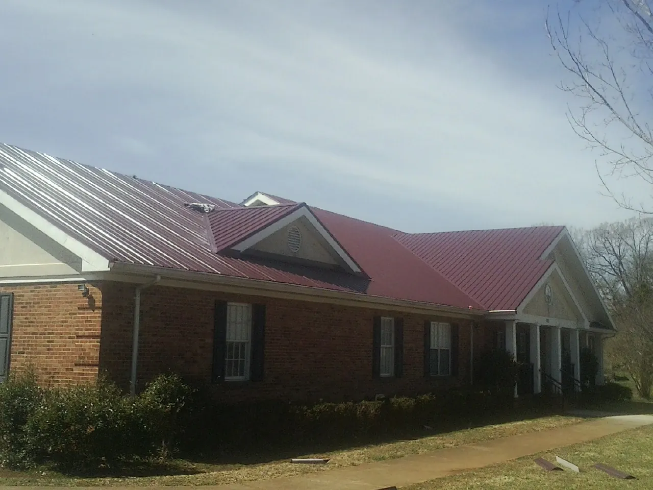 Red metal roof with gabled entries on a long brick building, from a Hail Damage Roof Repair job in Las Animas