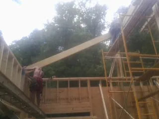 Carpenter raising a rafter beam on a new second story frame in Las Animas