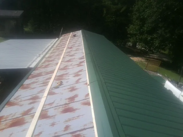 Old rusted panels beside newly installed green metal roofing — Wind Damage Roof Repair by Roofing Brothers in Las Animas