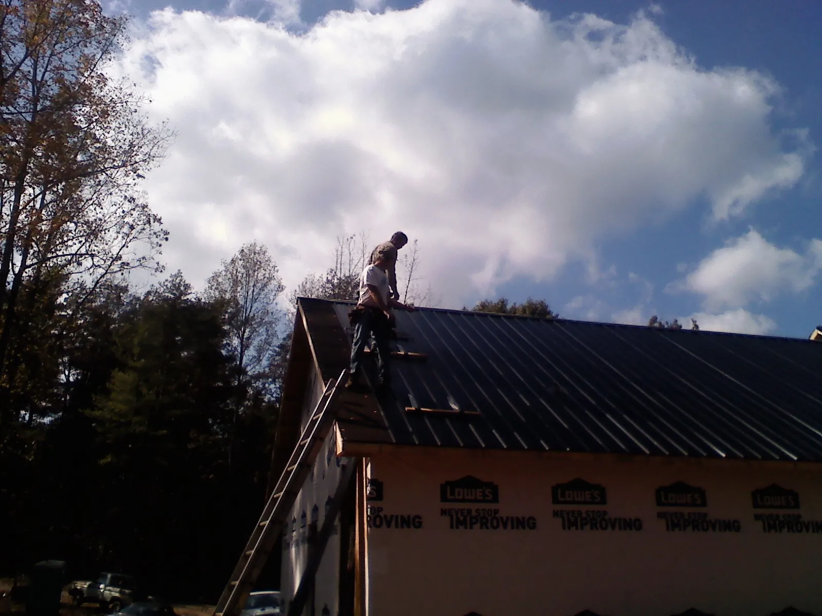 Roofer fastening dark metal panels high against a cloudy sky, from a Roof Inspection job in Las Animas