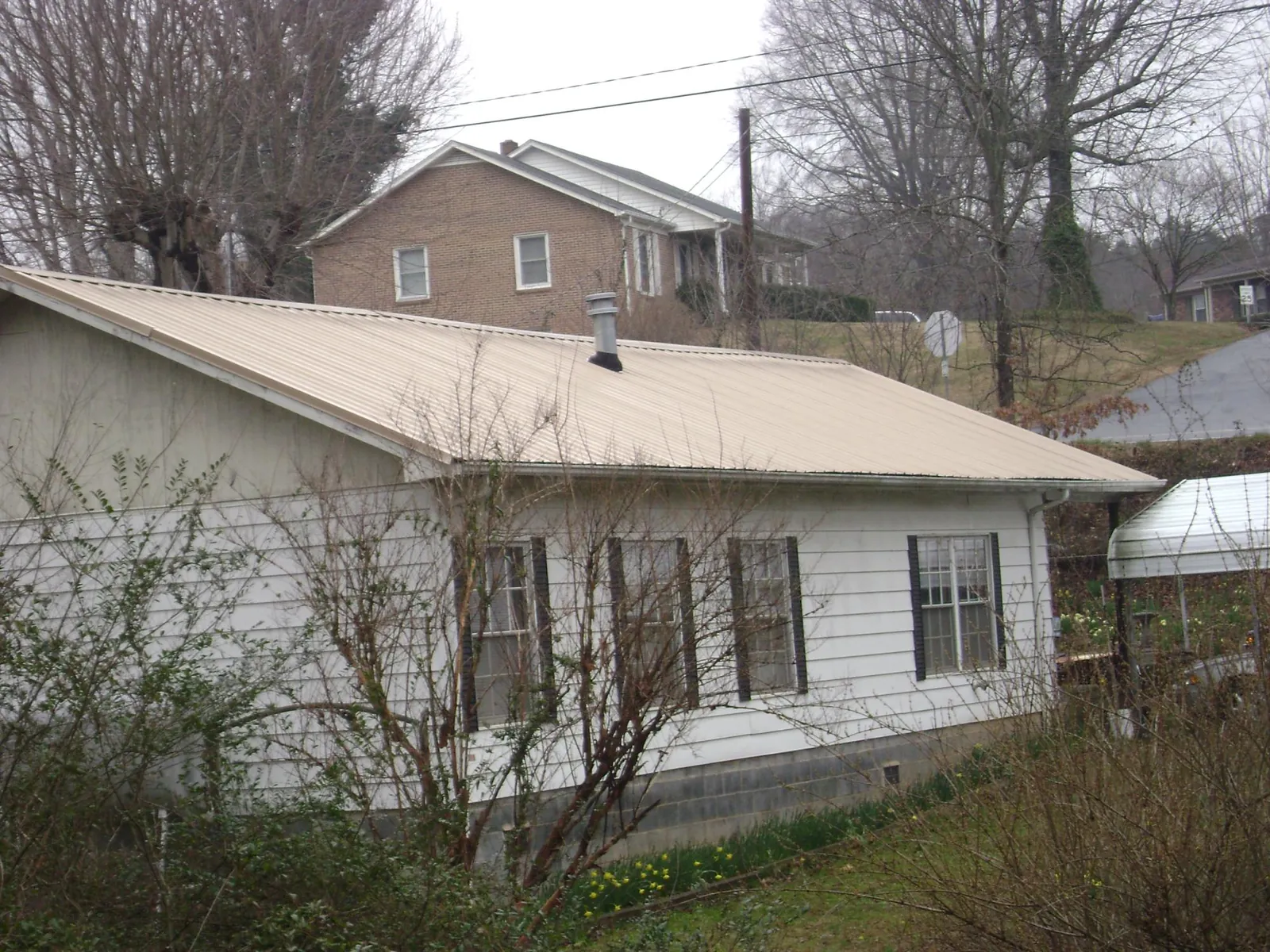 Tan metal roof on a white sided house set into a hillside — Commercial Roofing by Roofing Brothers in Las Animas